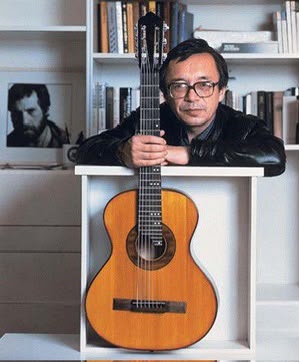 Юлий Ким с гитарой у книжных полок